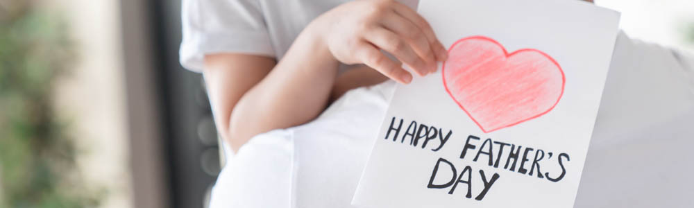 Close-up of child holding a Happy Father's Day card up in the arms of her dad Close-up of child holding a Happy Father's Day card up in the arms of her dad